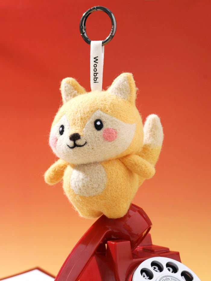 Cute wool fox keychain balancing on a retro telephone receiver, showcasing its sturdy needle-felted structure and playful design.