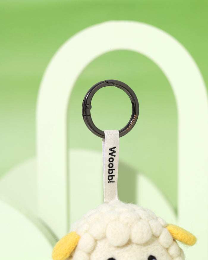 Close-up of durable black metal keychain ring and white woven Woobbi brand tag attached to a handcrafted wool sheep charm.