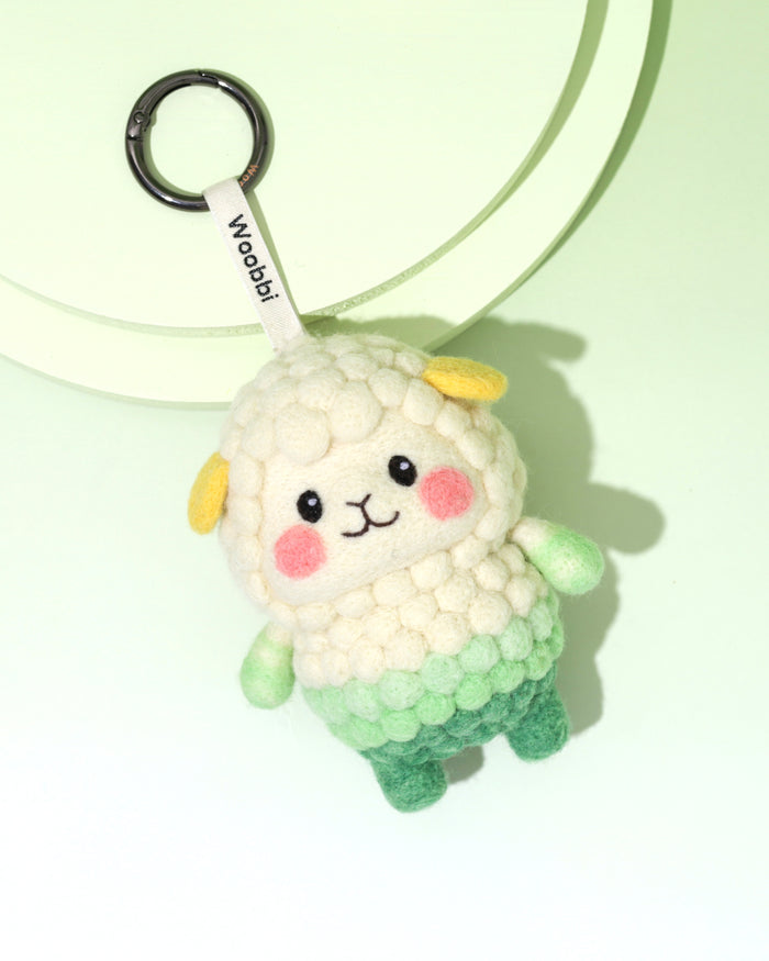 High-angle view of needle-felted sheep bag charm featuring a white 'popcorn' texture fleece fading into a green gradient body, with cute yellow ears.